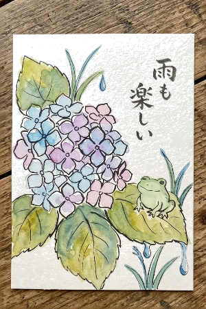 アジサイの塗り絵見本。明るいピンクや水色を使い、文字を添えた絵手紙風の仕上げ